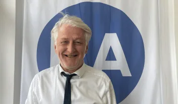 Smiling man with white hair, white shirt and tie.