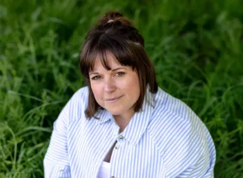Photo of lady sitting on grass wearing a blue and white striped shirt with brown hair